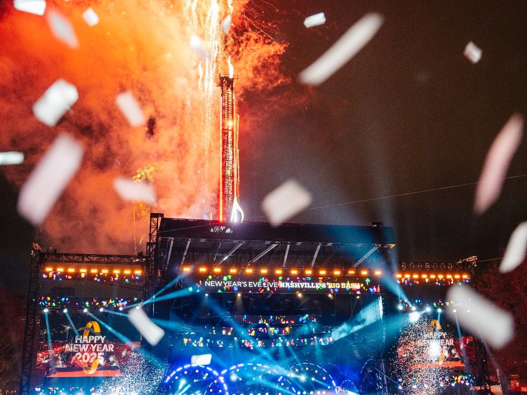 Fireworks explode above the Nashville Big Bash stage as confetti fills the air at midnight. The crowd celebrates the New Year with live performances and bright stage lights.