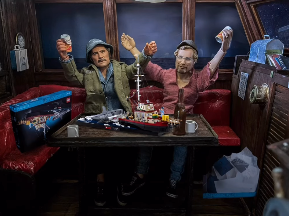 Diorama featuring two figures in a boat cabin celebrating with drinks, surrounded by red leather seating, a model ship on the table, and a LEGO box nearby