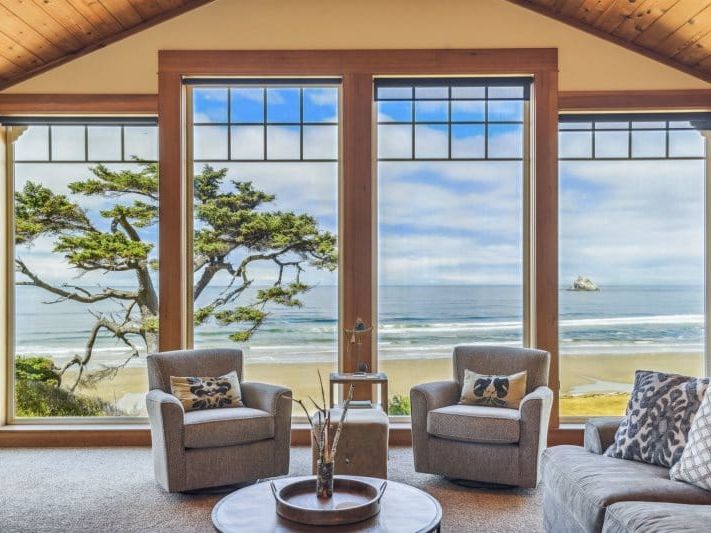 A modern coastal home featuring warm cedar siding, wide balconies, and a unique front garden sculpture. The bright driveway and open design create a relaxing atmosphere perfect for seaside getaways
