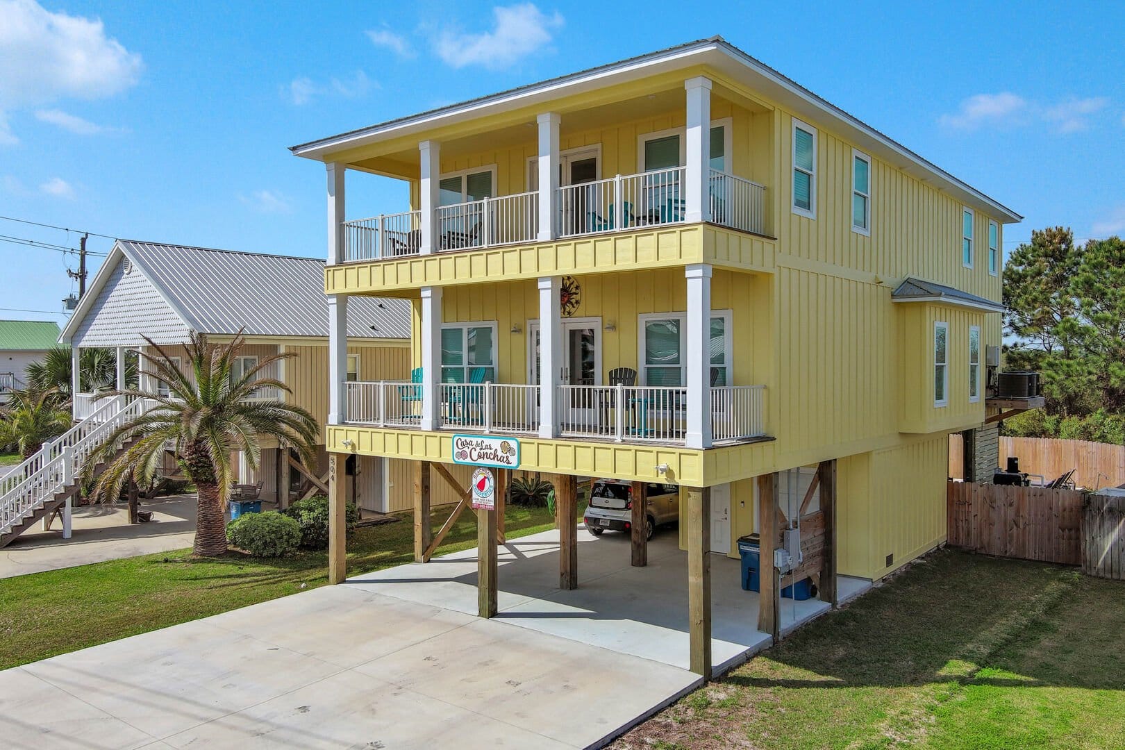 Bright yellow stilt beach house with two levels of balconies and covered parking below. Features white trim, outdoor seating, and a welcoming coastal style.