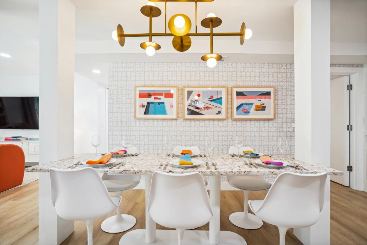 Chic modern dining area featuring a terrazzo-style table, white tulip chairs, and colorful napkins that pop against a geometric wallpaper backdrop.