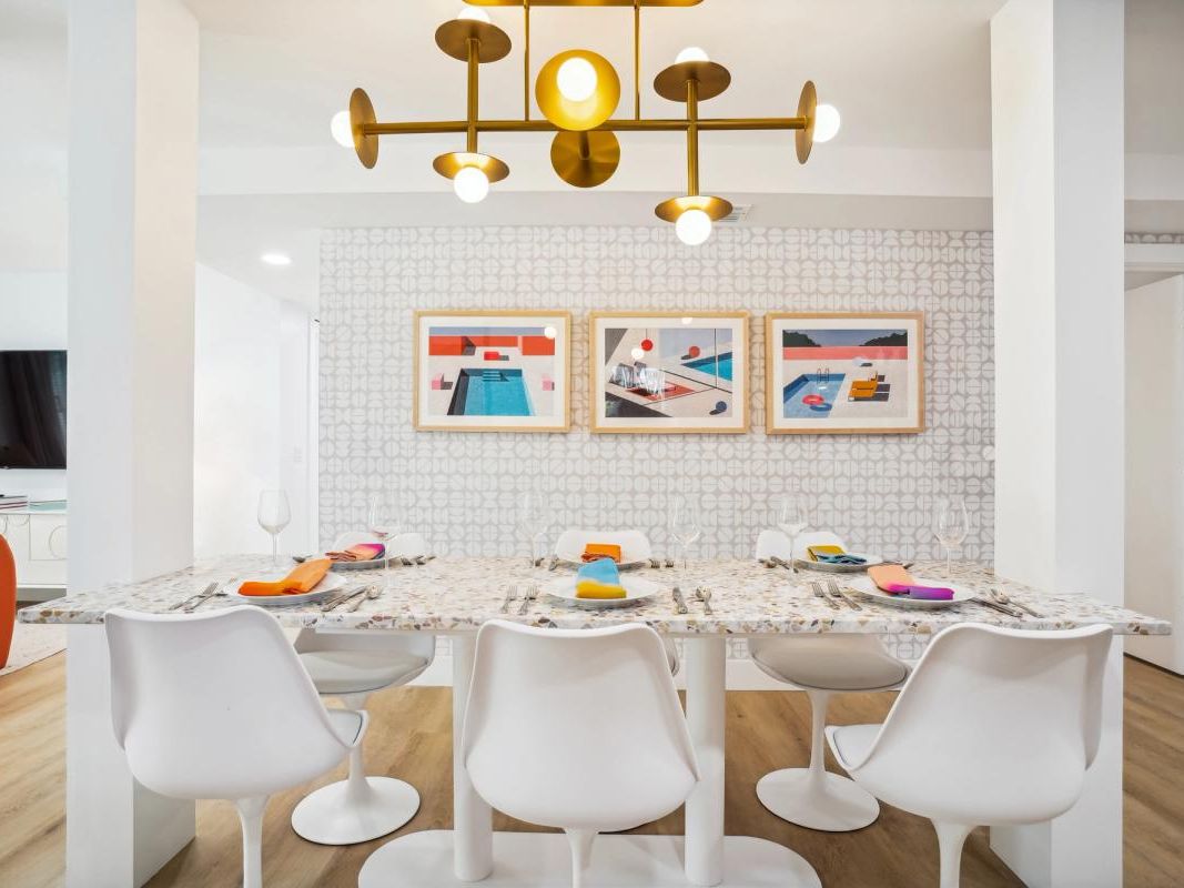 Chic modern dining area featuring a terrazzo-style table, white tulip chairs, and colorful napkins that pop against a geometric wallpaper backdrop.