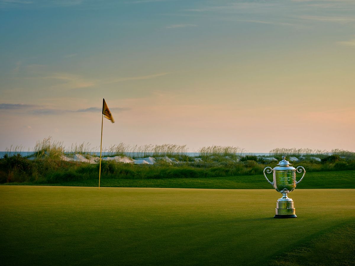 A stunning view of Kiawah Island Golf Course at sunset, with a championship trophy placed on the green near the flag. The ocean waves and sea grass in the background make this world-class course a favorite for golf lovers.