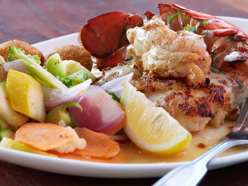 Grilled lobster tail and fish served with mixed sautéed vegetables and a lemon wedge. A seafood lover’s dream dish at Pompano Joe’s.
