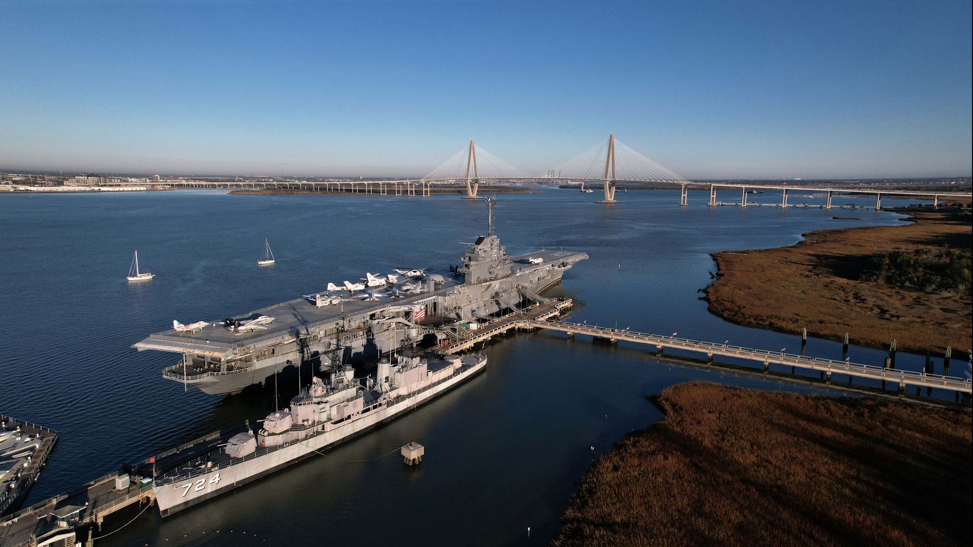 Patriots Point Naval & Maritime Museum features a massive aircraft carrier and naval ships docked along the Charleston harbor. The iconic Ravenel Bridge rises in the distance, creating one of the most recognizable views in South Carolina.