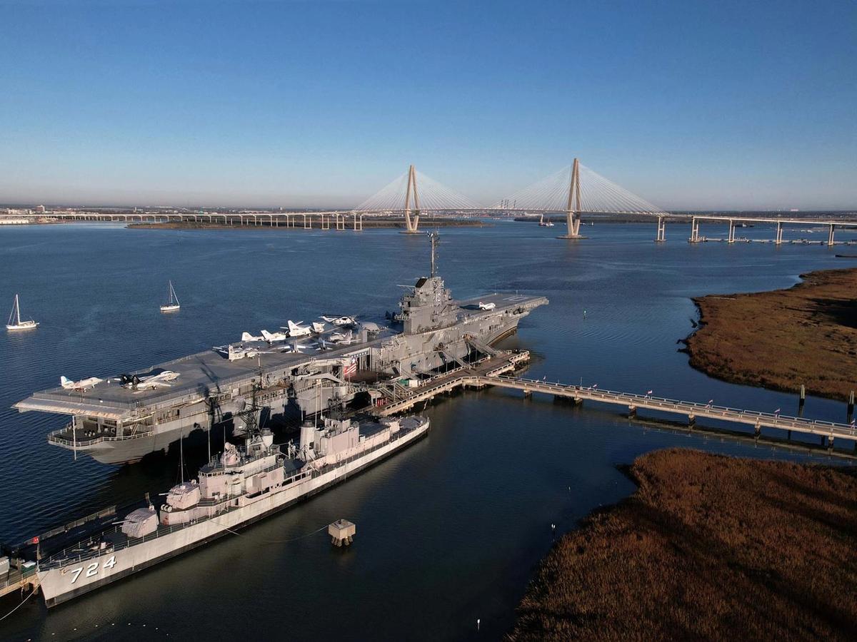 Patriots Point Naval & Maritime Museum features a massive aircraft carrier and naval ships docked along the Charleston harbor. The iconic Ravenel Bridge rises in the distance, creating one of the most recognizable views in South Carolina.