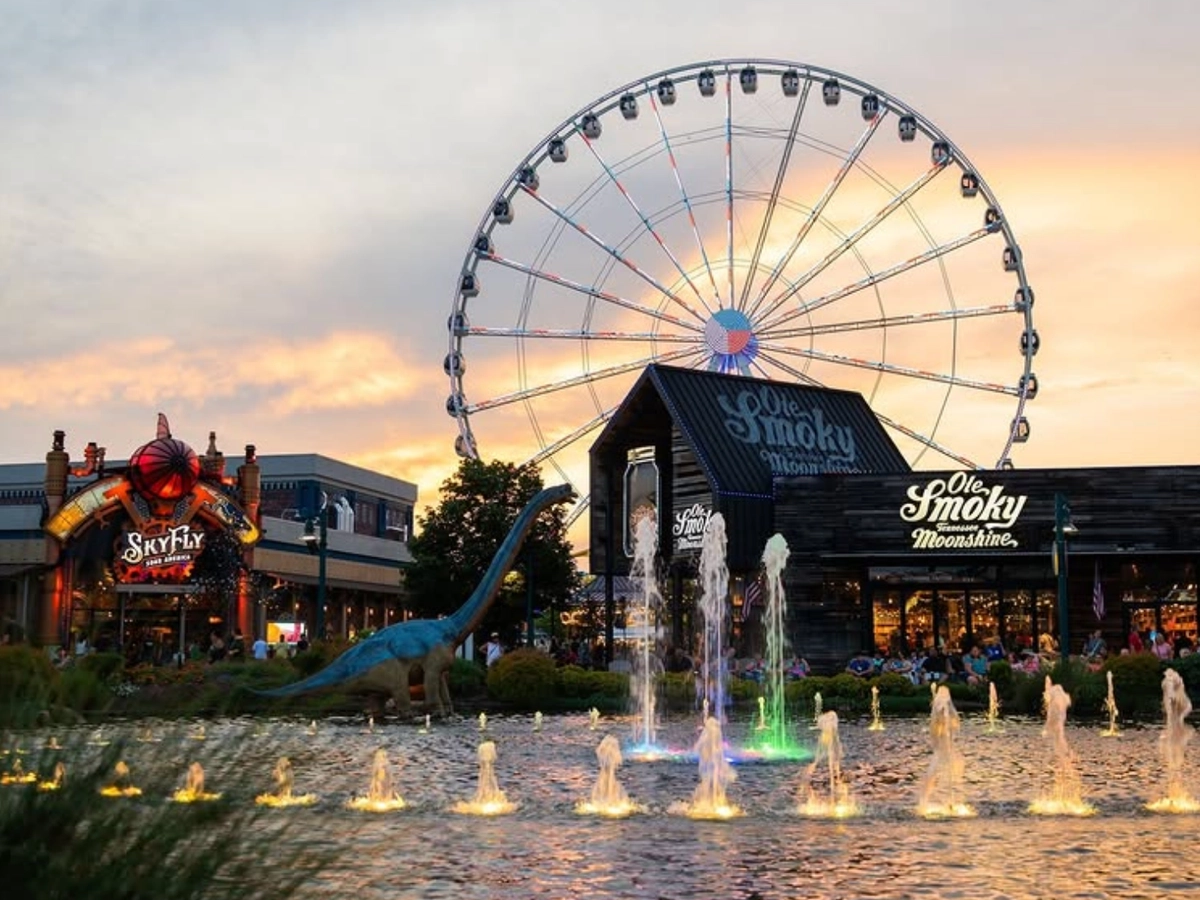 A large Ferris wheel towers over The Island in Pigeon Forge, with fountains, shops, and attractions glowing at sunset.