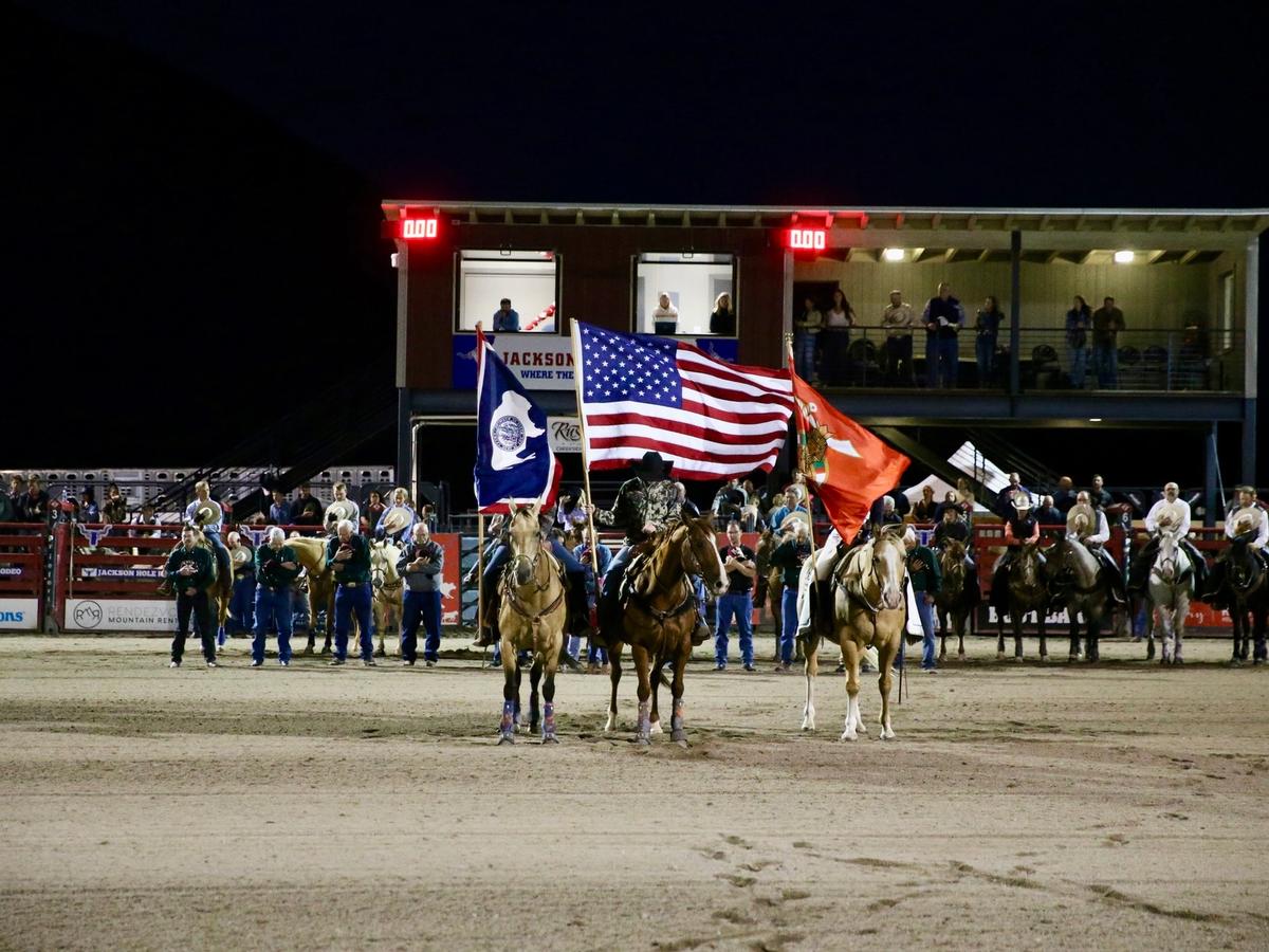 Riders carry flags during a nighttime event at the Jackson Hole Rodeo, with crowds watching from the stands. The rodeo highlights local Western traditions and community spirit. It’s a classic summer experience in Jackson Hole.