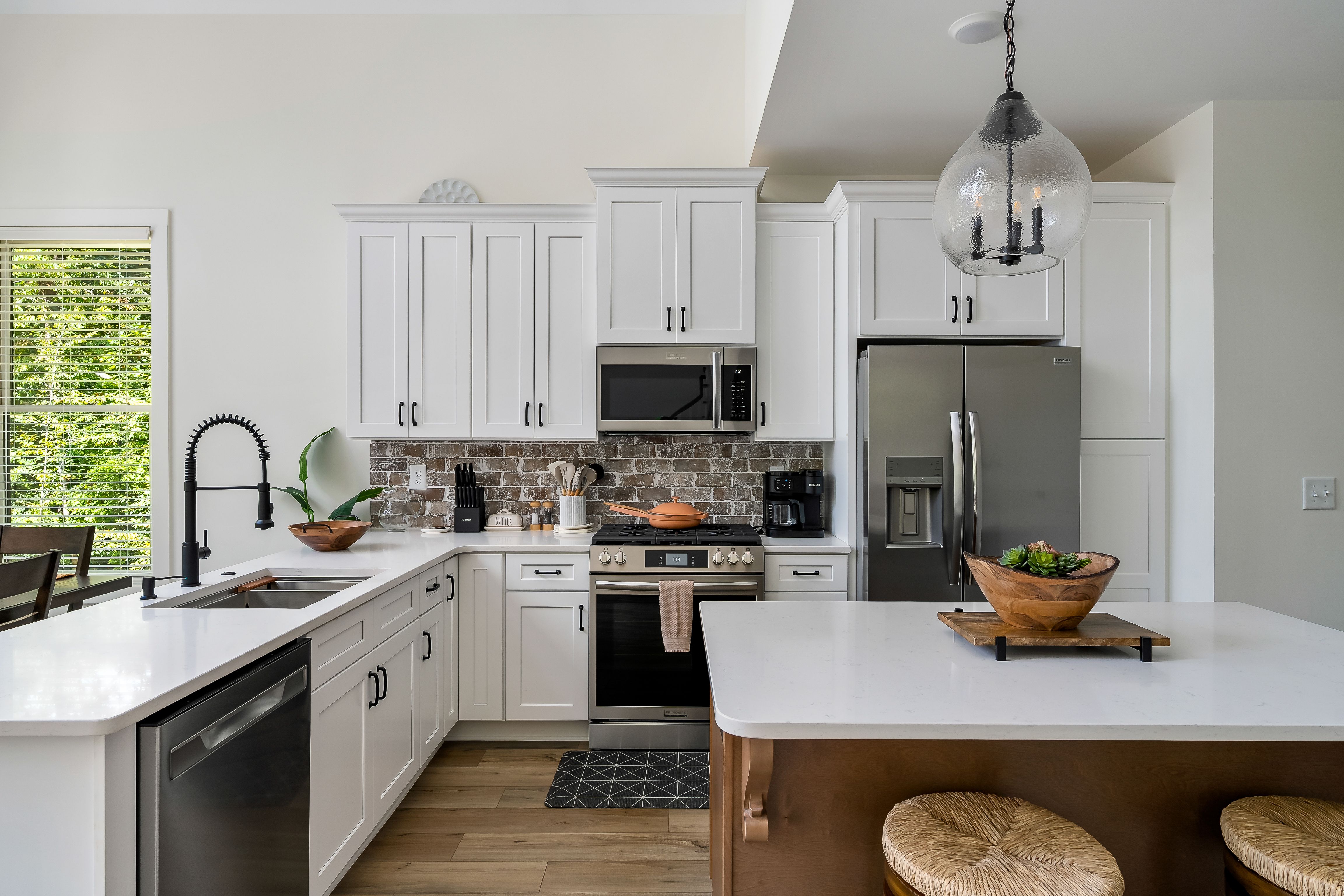 Bright and modern kitchen with white cabinetry, stainless steel appliances, a brick backsplash, and a large island with natural wood accents.