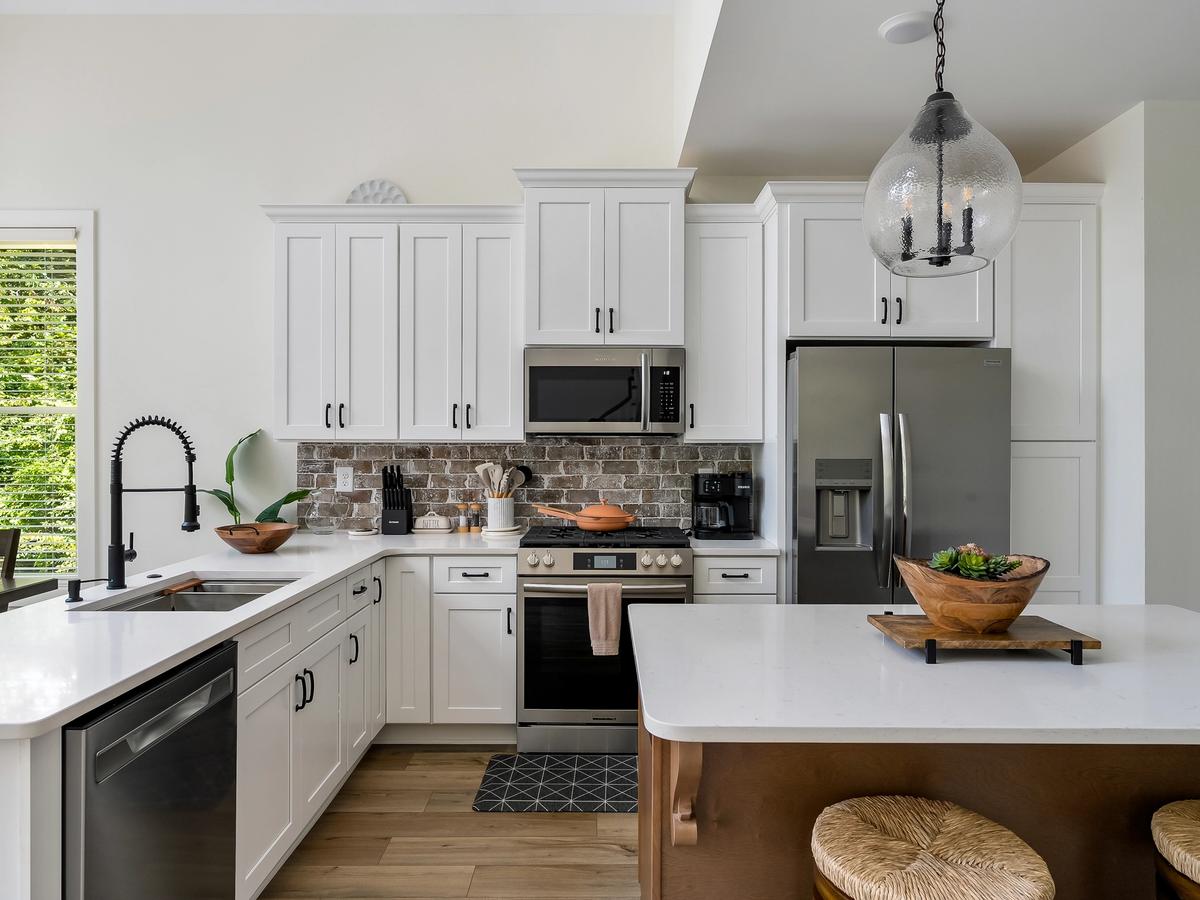 Bright and modern kitchen with white cabinetry, stainless steel appliances, a brick backsplash, and a large island with natural wood accents.