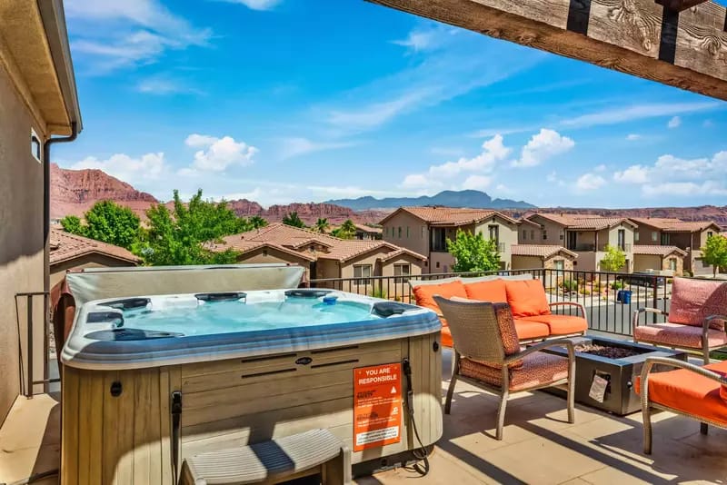 Rooftop patio with a hot tub, orange cushioned seating, and scenic red rock mountain views in the distance.