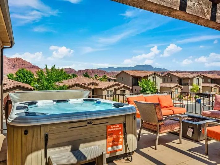 Rooftop patio with a hot tub, orange cushioned seating, and scenic red rock mountain views in the distance.