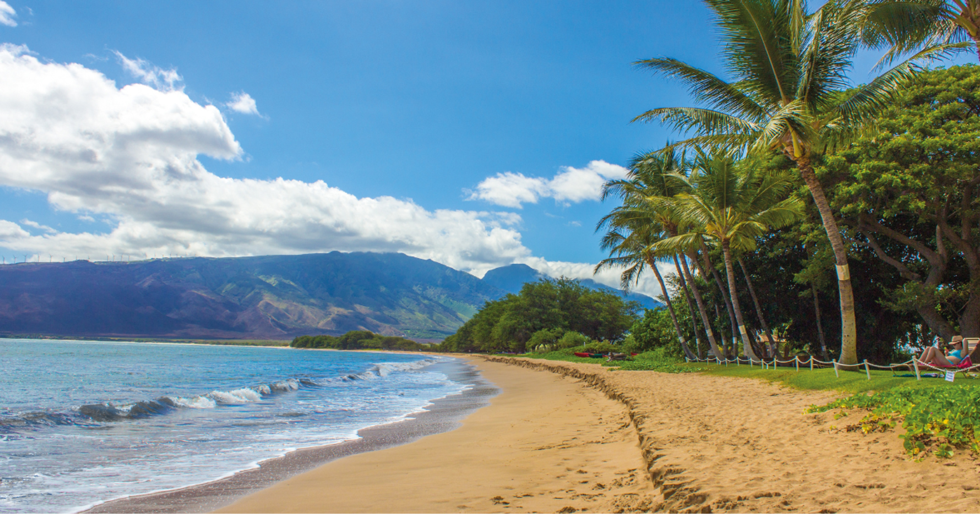 A quiet beach with soft sand, gentle waves, and a rocky cliff in the distance under a bright blue sky. This untouched shoreline is perfect for sunbathing, swimming, or a morning walk.