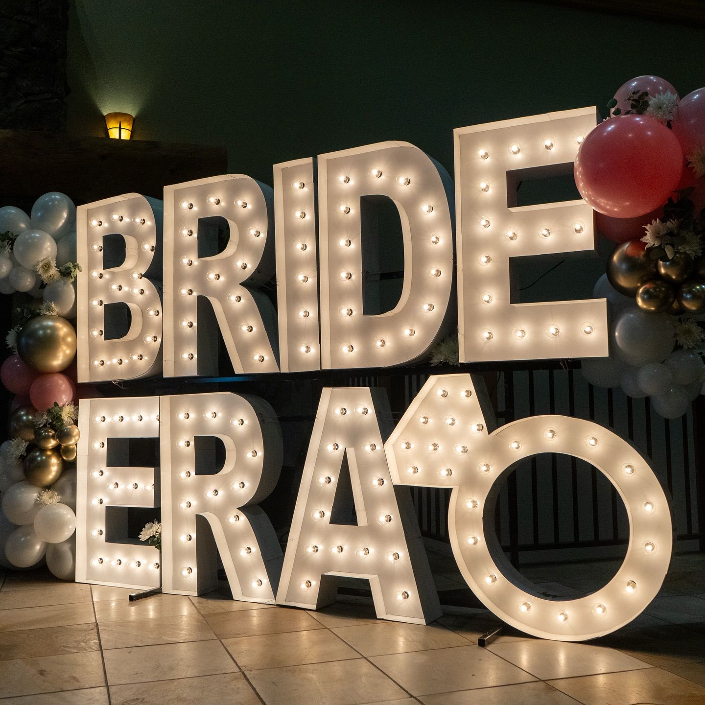 Large marquee lights spelling “BRIDE ERA” glow warmly against a stylish backdrop of balloons and soft lighting. The display creates a romantic, Instagram-worthy scene that celebrates love and modern bridal trends.