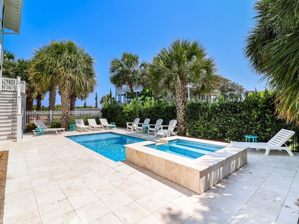 A modern beachfront mansion lined with palm trees and floor-to-ceiling windows faces the water. Its clean design and open terraces reflect the exclusive lifestyle offered by The 100 Collection homes.