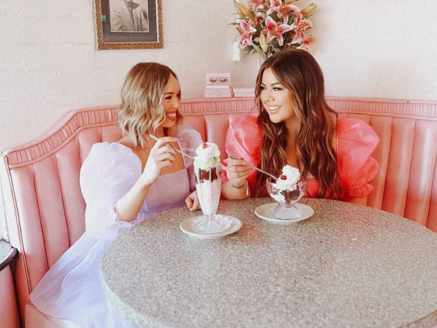 Two girls in pink poofy dresses sitting side by side eating ice cream sundaes at cute ice cream restaurant