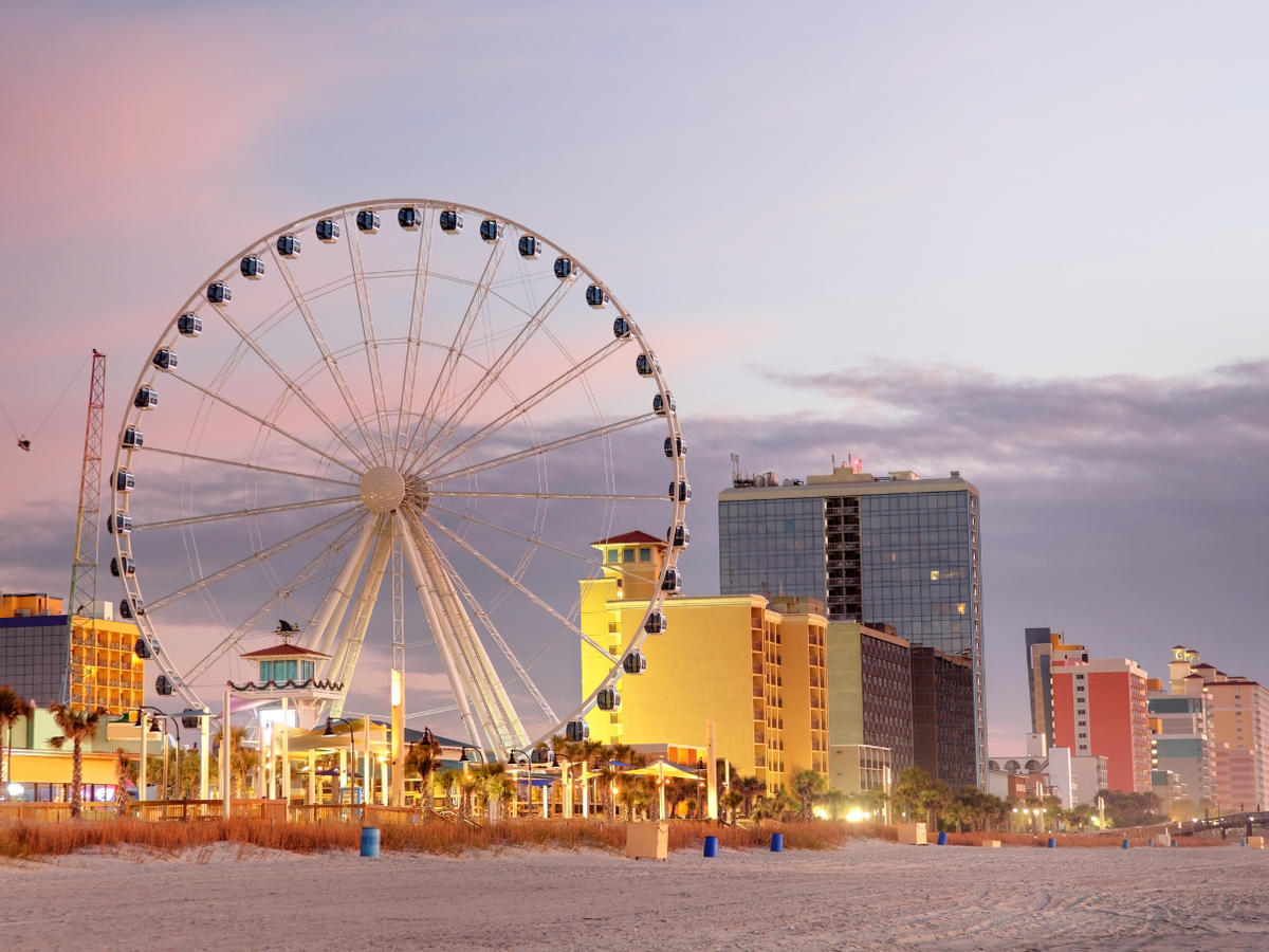 Wheel and lit up businesses and buildings at myrtle beach with beach in the foreground