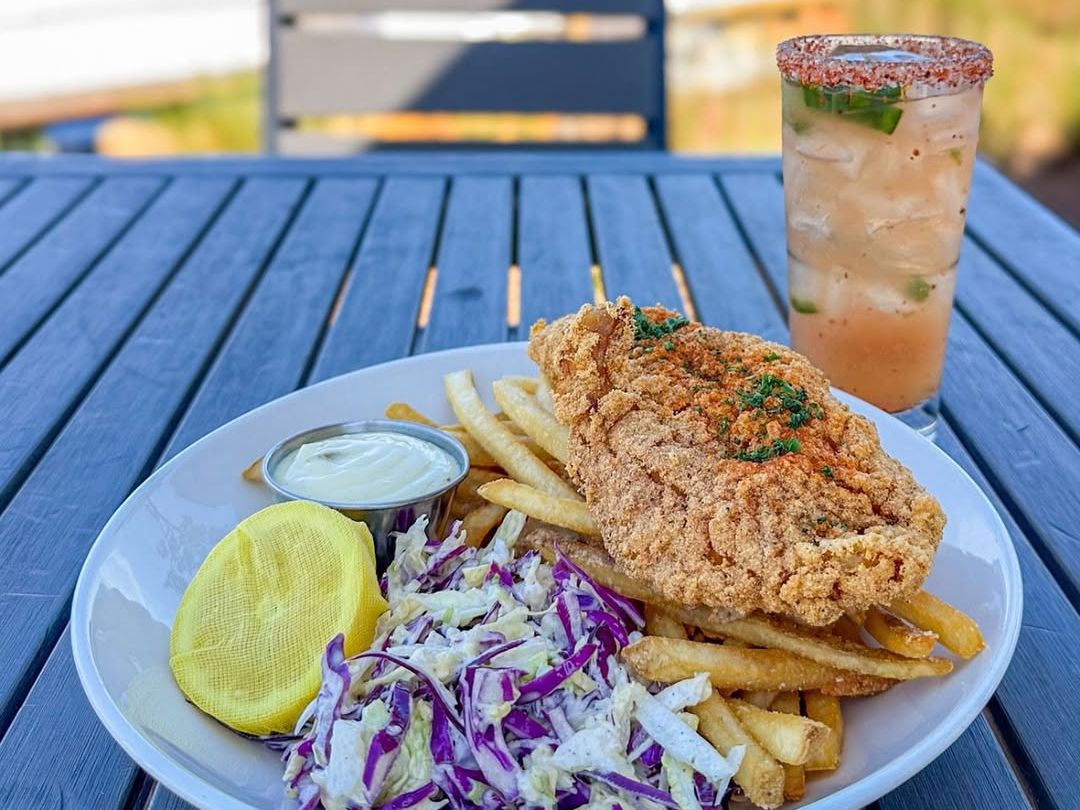 Golden fried fish served with fries, coleslaw, and tartar sauce, paired with a chilled cocktail. A classic seafood basket with marina views in the background.