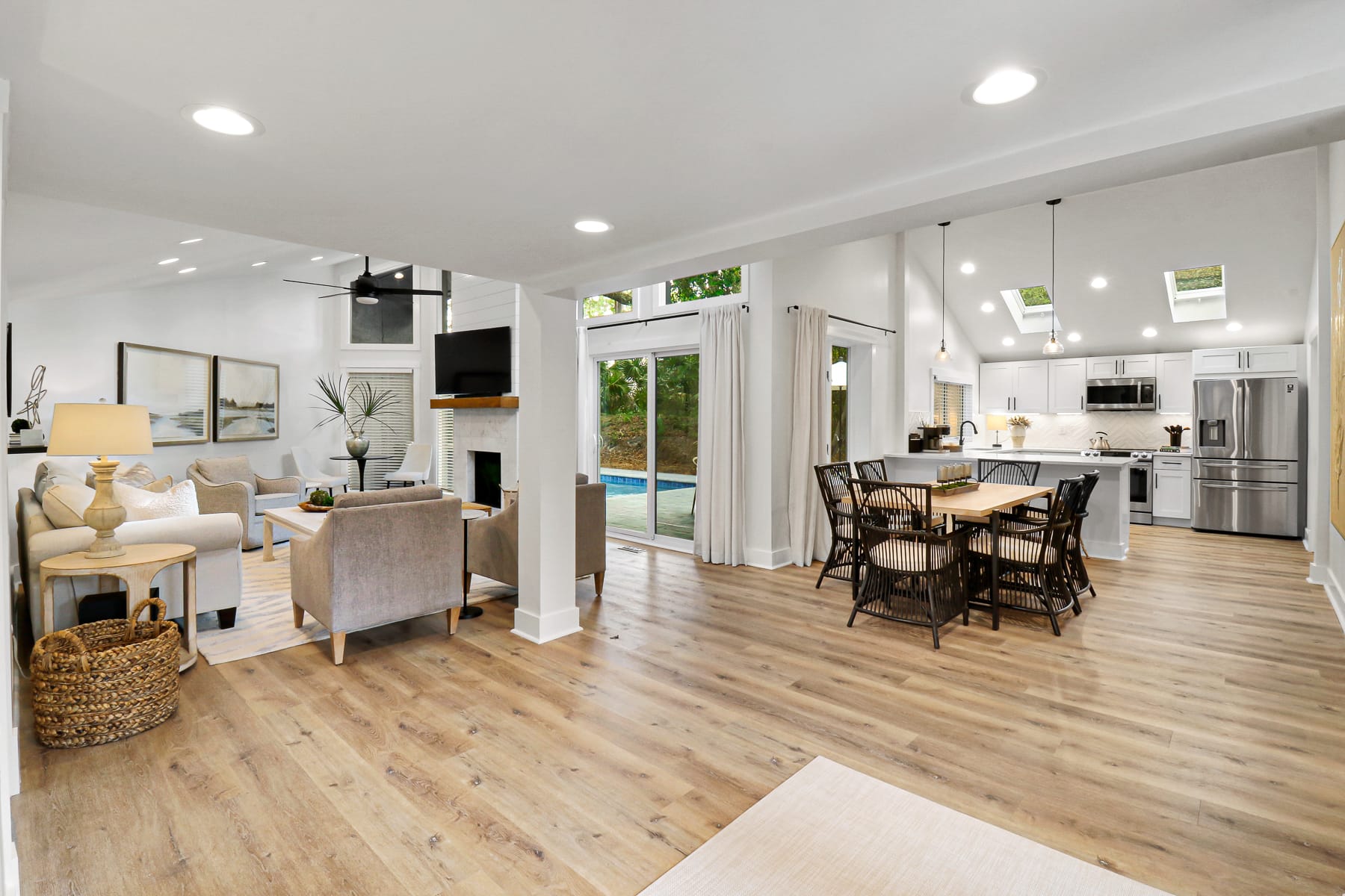 A super stylish, fully renovated coastal home features a bright open-plan living area with modern white sofas, crisp kitchen finishes, and a private pool with custom evening lightscaping, set against serene lagoon and golf views