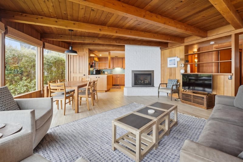 A cozy coastal cabin with warm wood interiors, large windows, and a fireplace. The inviting living space pairs classic beach style with modern comfort for a relaxing retreat near the ocean.
