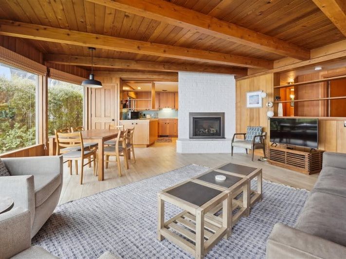 A cozy coastal cabin with warm wood interiors, large windows, and a fireplace. The inviting living space pairs classic beach style with modern comfort for a relaxing retreat near the ocean.