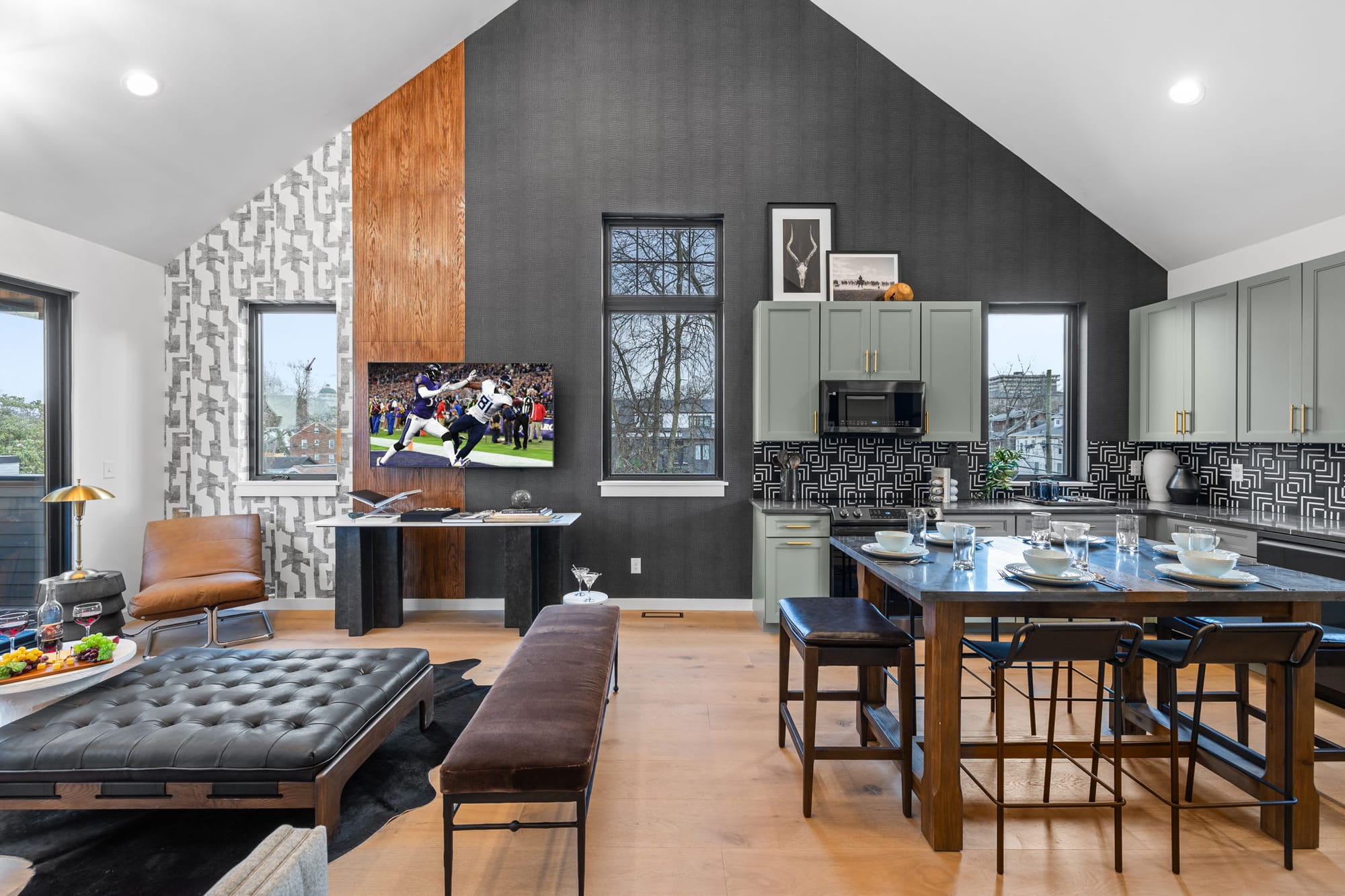 Modern loft-style living and dining space with vaulted ceilings, dark accent wall, sleek kitchen, and contemporary lounge seating.