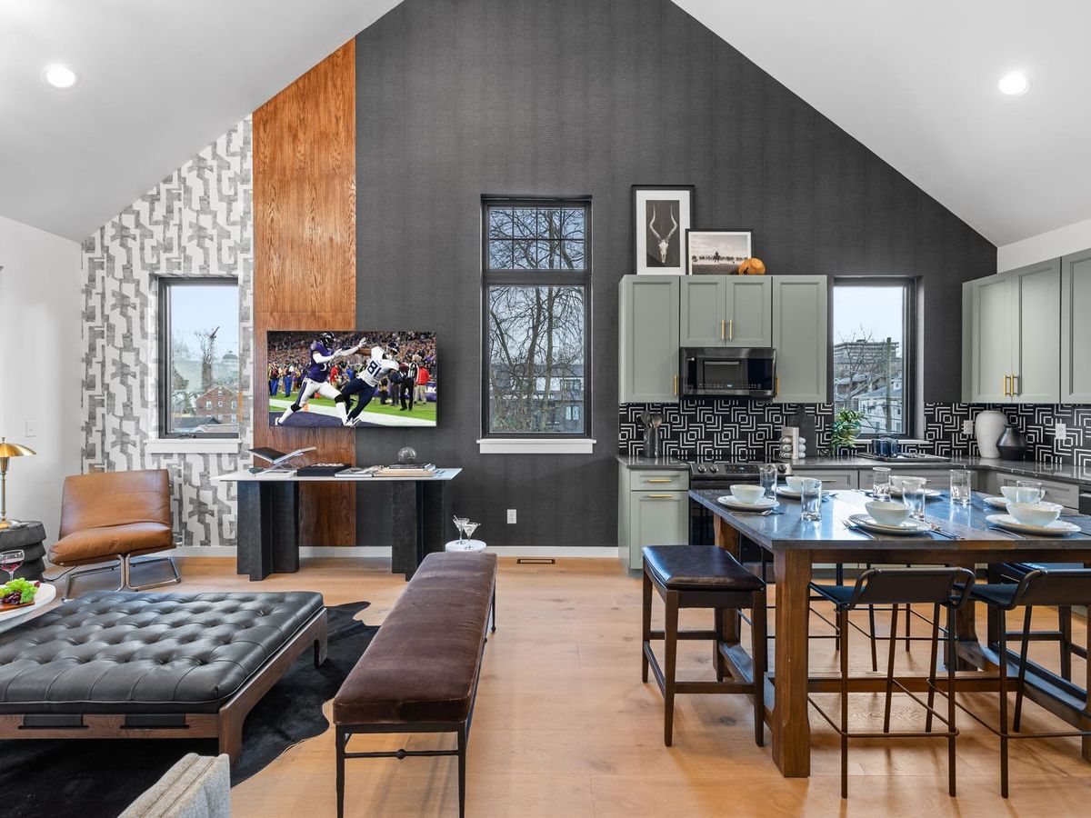 Modern loft-style living and dining space with vaulted ceilings, dark accent wall, sleek kitchen, and contemporary lounge seating.