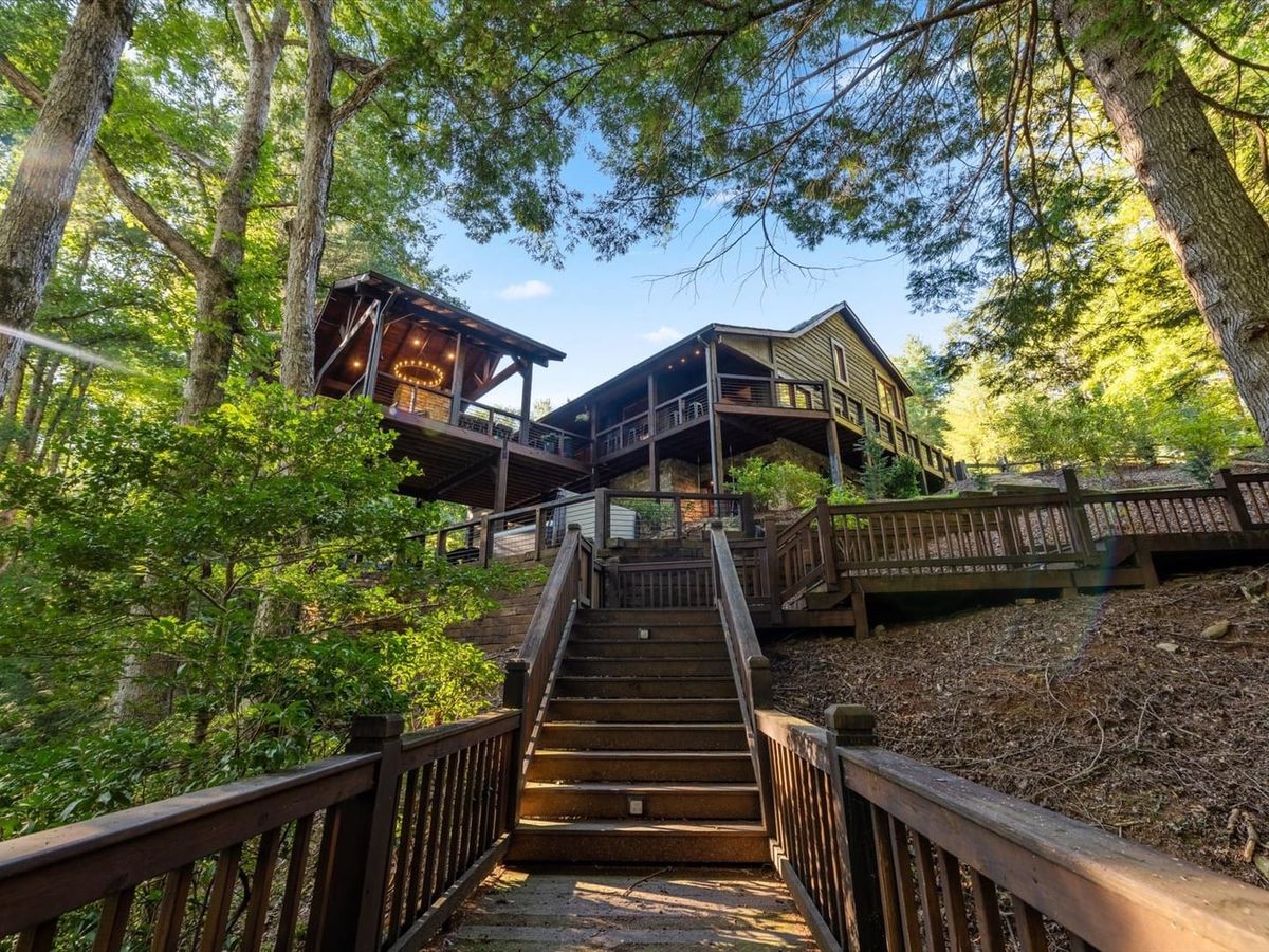 A stunning multi-level mountain lodge surrounded by tall trees in Blue Ridge, Georgia. Expansive wooden decks offer forest views and cozy outdoor spaces perfect for gathering with family and friends.