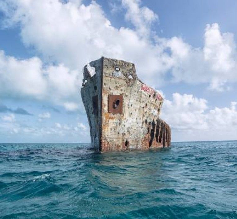 A shipwreck rising above clear blue water in The Bahamas, surrounded by open sea and bright skies. This historic wreck is a popular spot for snorkeling and diving adventures. It offers a unique way to explore marine life and underwater history.
