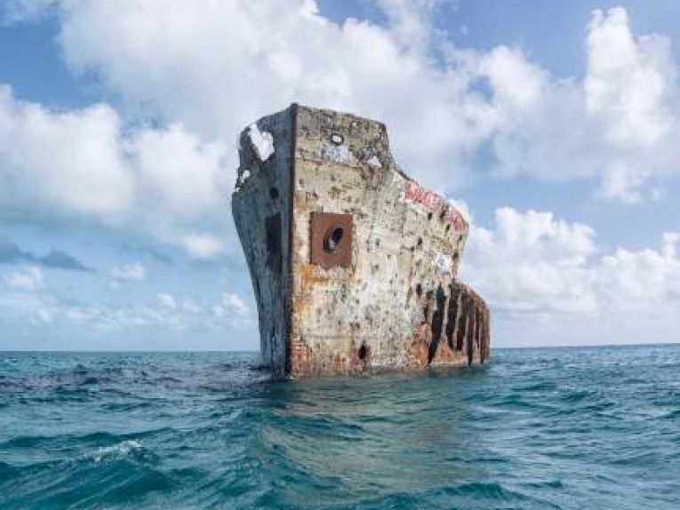 A shipwreck rising above clear blue water in The Bahamas, surrounded by open sea and bright skies. This historic wreck is a popular spot for snorkeling and diving adventures. It offers a unique way to explore marine life and underwater history.