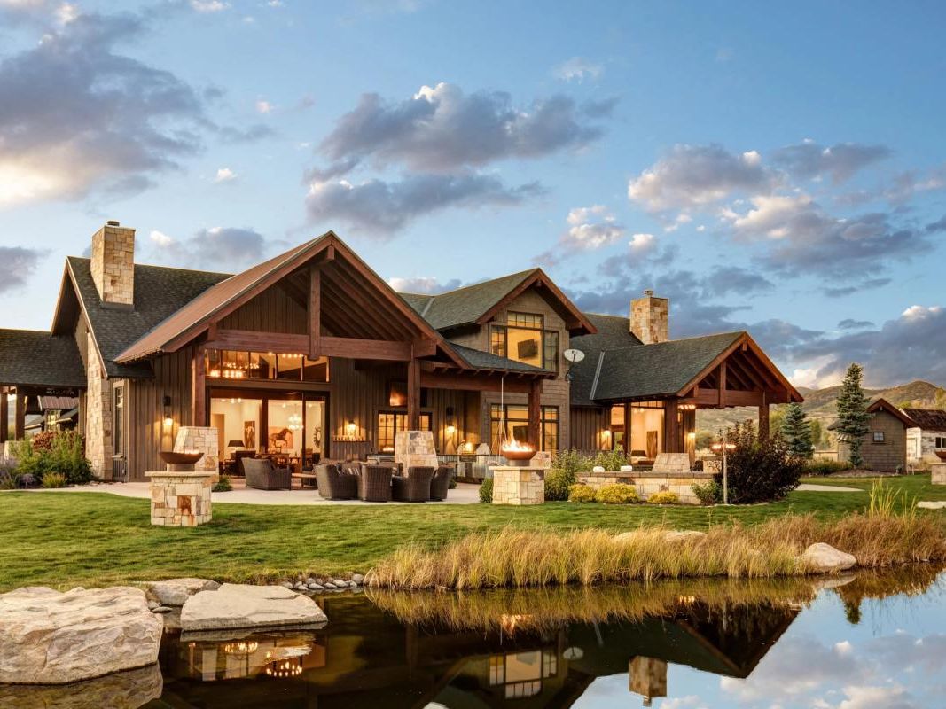 A stunning luxury mountain lodge beside a peaceful pond with expansive outdoor seating, glowing fire pits, and lodge-style architecture. Ideal for group getaways in a scenic alpine setting.