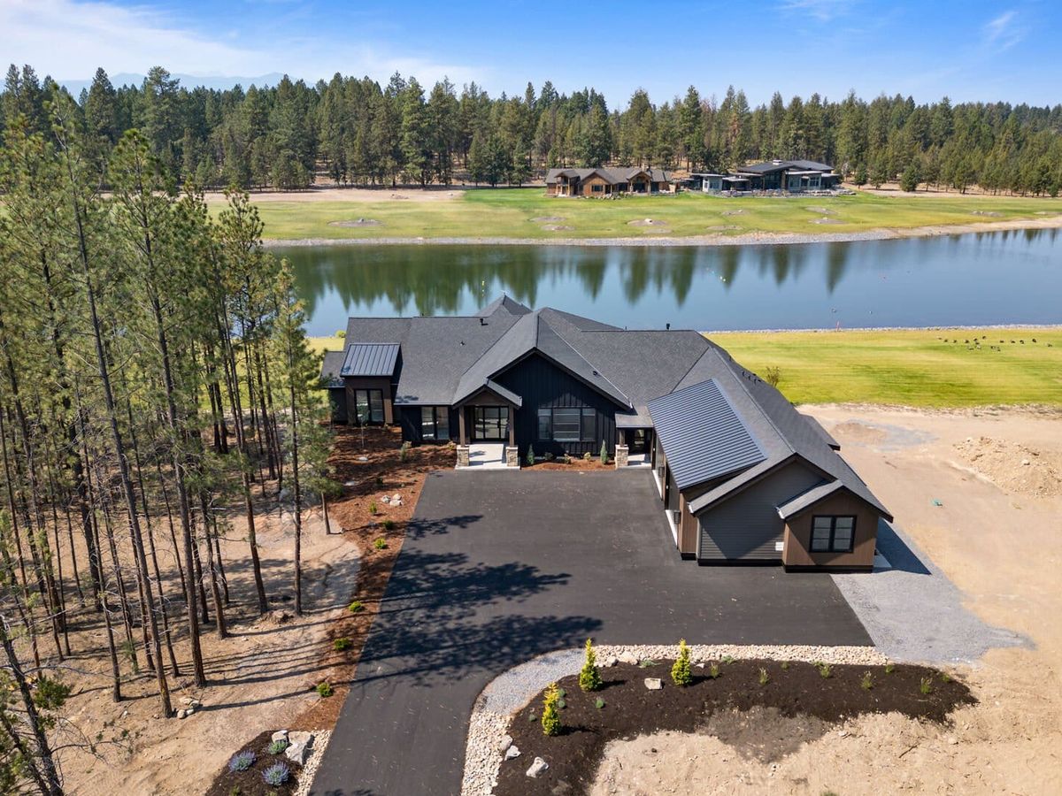 A luxurious lakeside property with a wide driveway, surrounded by tall pines and overlooking a peaceful waterfront. The home’s elegant design and stunning views make it a perfect retreat for large groups.