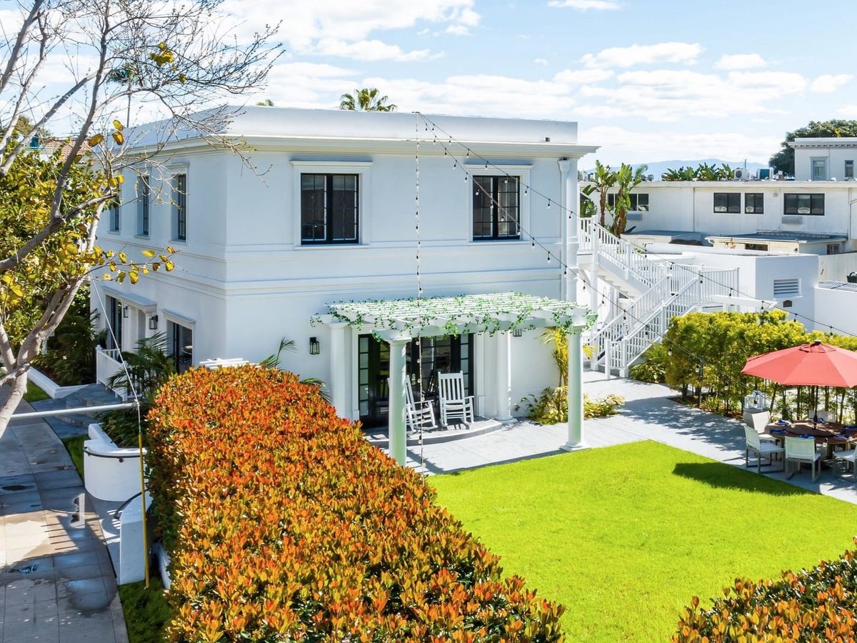 Coronado Crown Villas is a stunning white two-story home with a large green lawn, shaded patio, and outdoor dining space under a red umbrella. Perfect for families and groups, this elegant vacation rental offers a blend of charm and comfort just minutes from the beach.