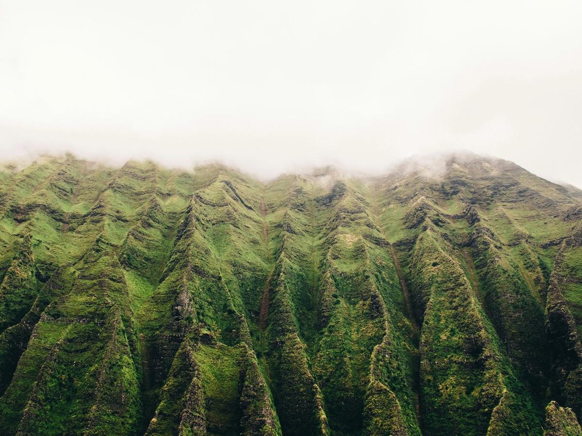 Steep green ridges of Kauai’s Nā Pali Coast rise into low-hanging clouds, creating a dramatic, mist-covered mountain landscape.