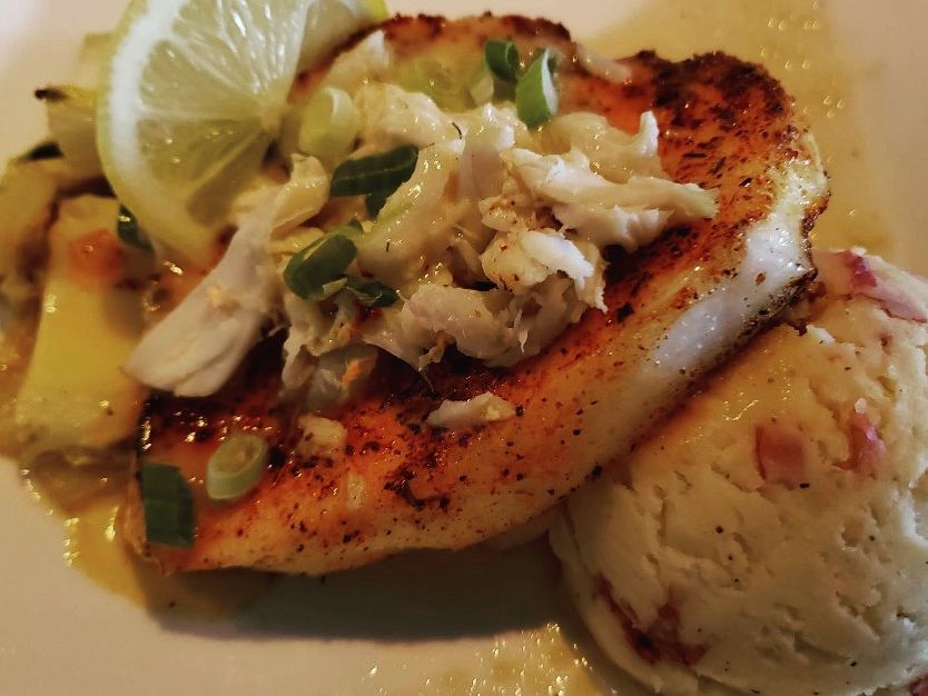 Grilled fish topped with crab meat, green onions, and a slice of lemon, served with mashed potatoes. A comforting seafood entrée packed with coastal flavor.