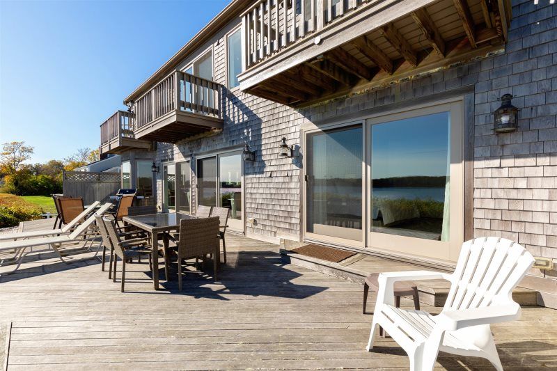 Spacious waterfront deck with weathered wood siding, outdoor dining and lounge seating, sliding glass doors, and upper-level balconies overlooking tranquil water views.