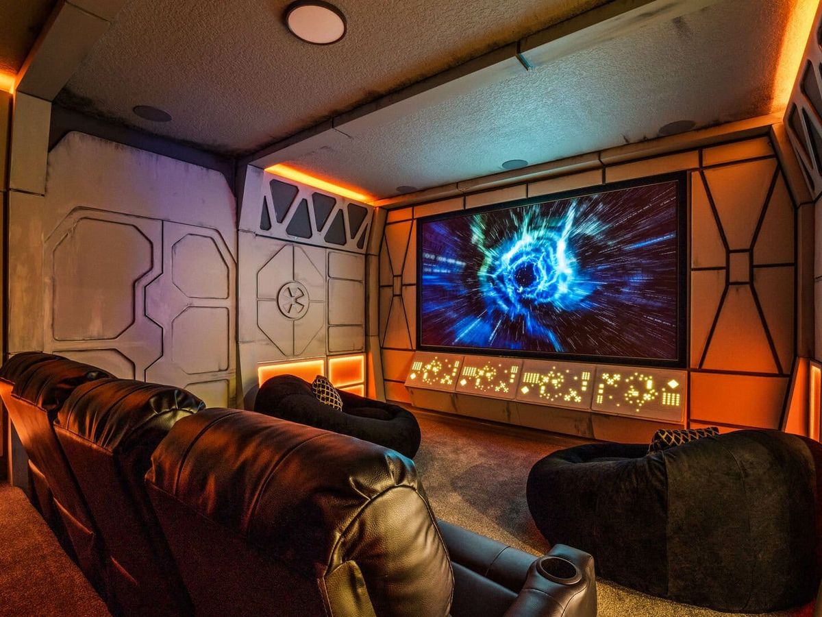 Themed movie room with black leather seats, bean bags, and astral scene on movie screen