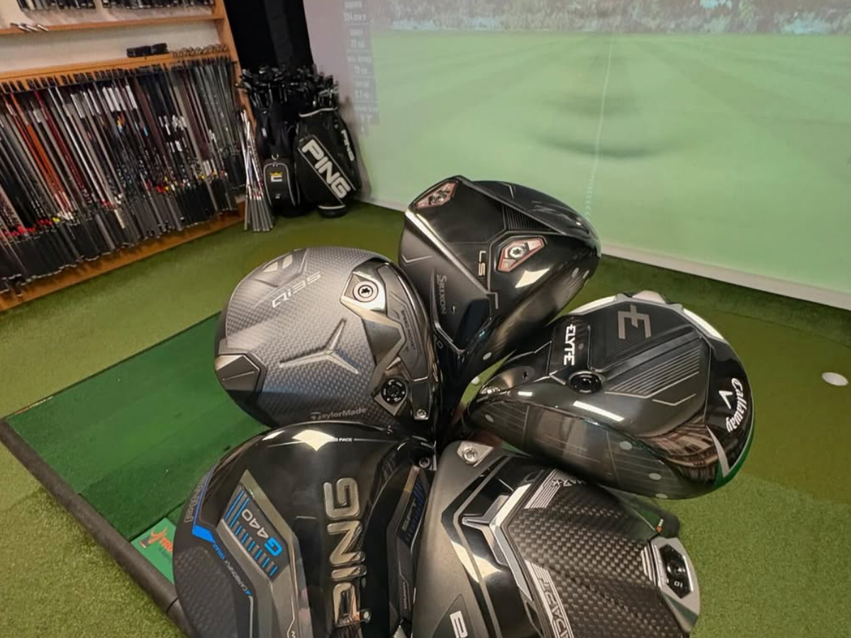 Golf clubs with golf screen and indoor putt in the background