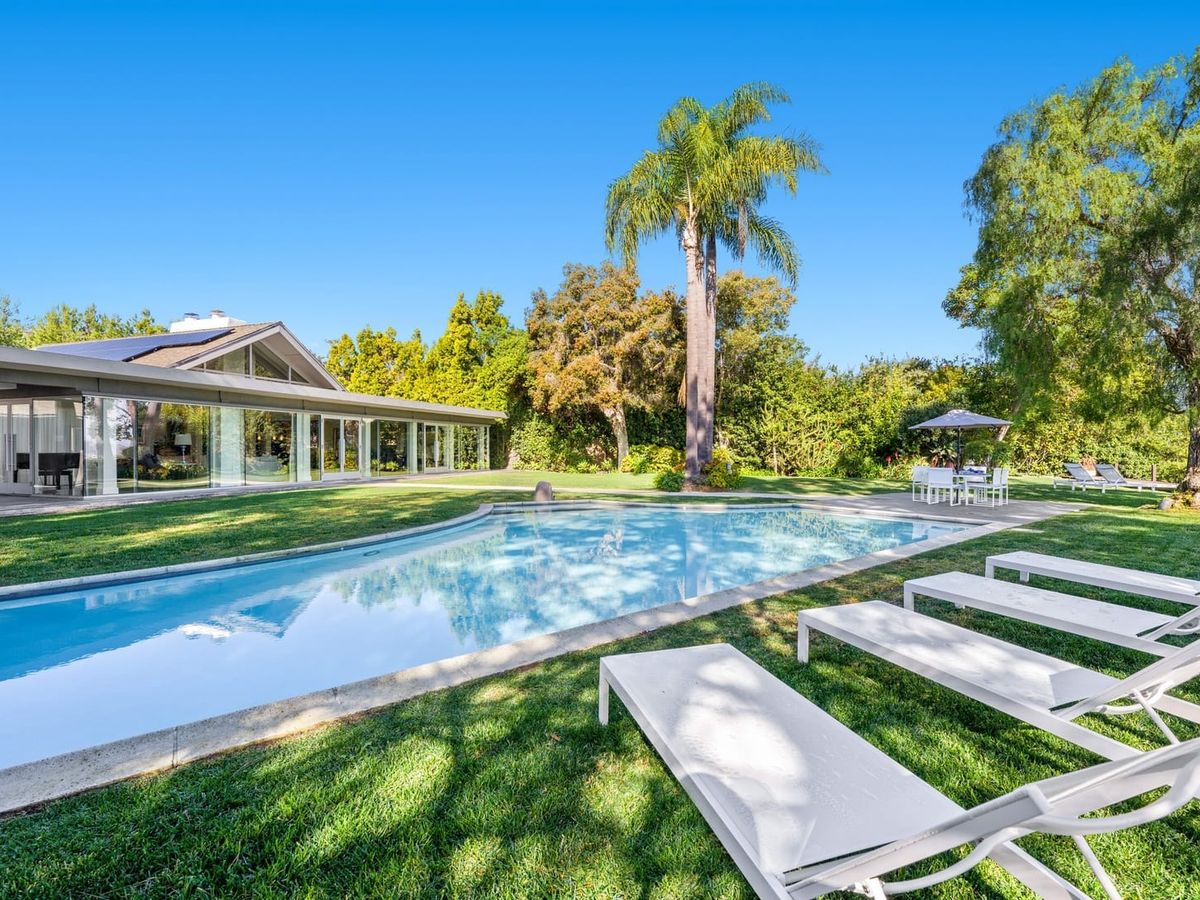 Endless Vistas vacation home features a stunning modern design with glass walls, a spacious lawn, and a sparkling private pool surrounded by lounge chairs. Perfect for large groups, this San Diego retreat offers space, comfort, and luxury.