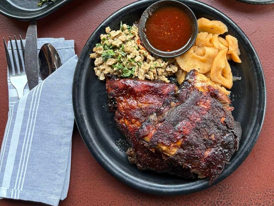 A hearty plate of barbecue ribs is paired with savory sides, including seasoned grains and stewed apples. Alma Bea’s Southern-inspired cooking highlights bold flavors and comforting presentation