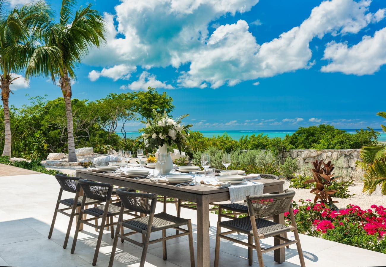 Beachwood Villa offers an outdoor dining area surrounded by tropical gardens with clear views of the turquoise Caribbean Sea. The shaded patio creates a beautiful setting for meals and relaxed evenings during an island vacation.