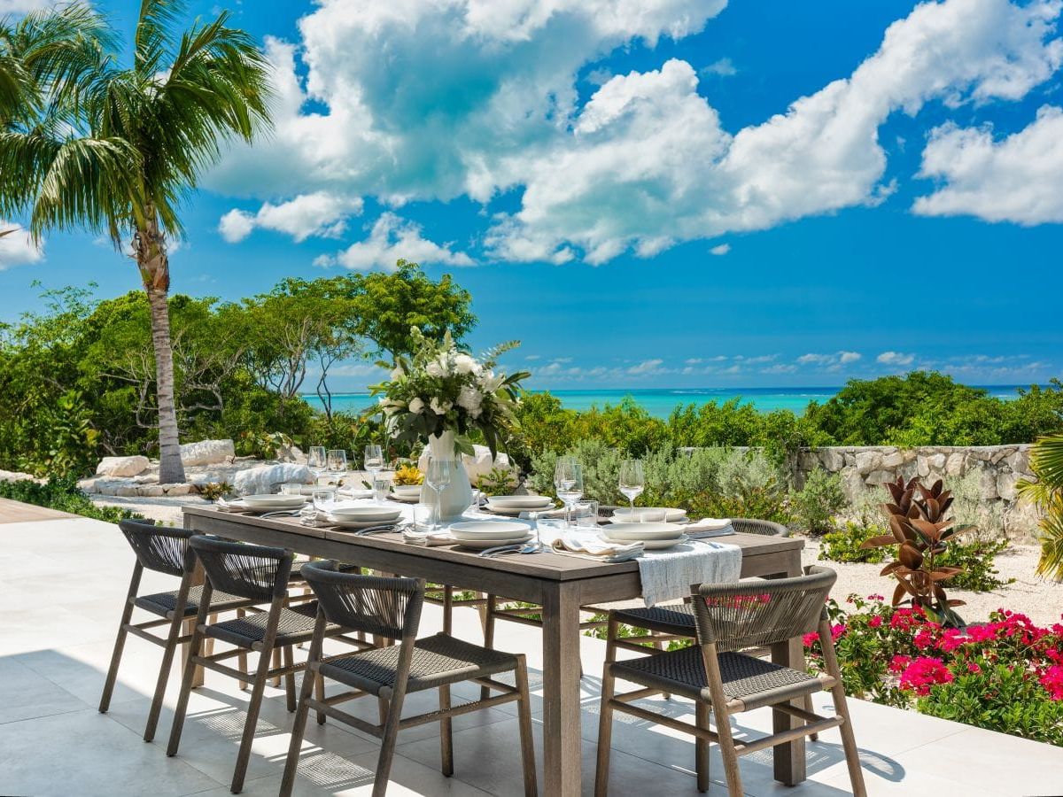 Beachwood Villa offers an outdoor dining area surrounded by tropical gardens with clear views of the turquoise Caribbean Sea. The shaded patio creates a beautiful setting for meals and relaxed evenings during an island vacation.
