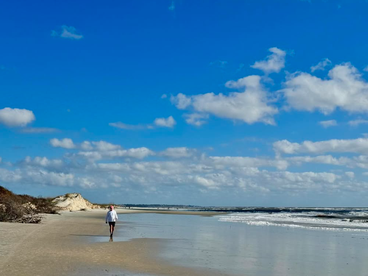 Person walking alone on beautiful beach with light clouds and blue skies overhead