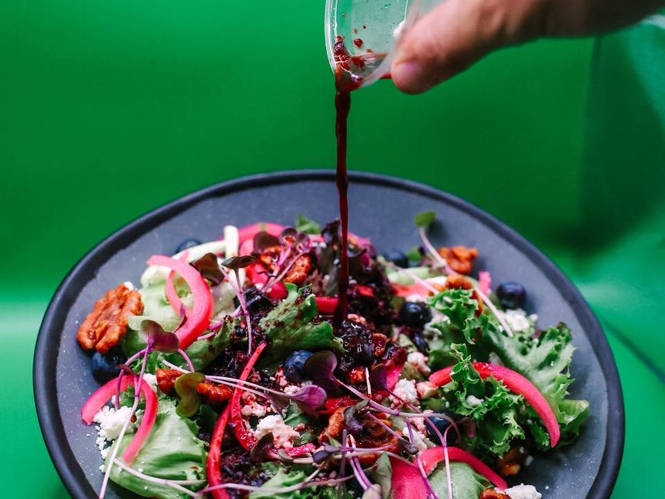 A colorful beet salad with pickled onions, blueberries, walnuts, and fresh greens being topped with a rich berry vinaigrette. A fresh and healthy option full of bold flavors.