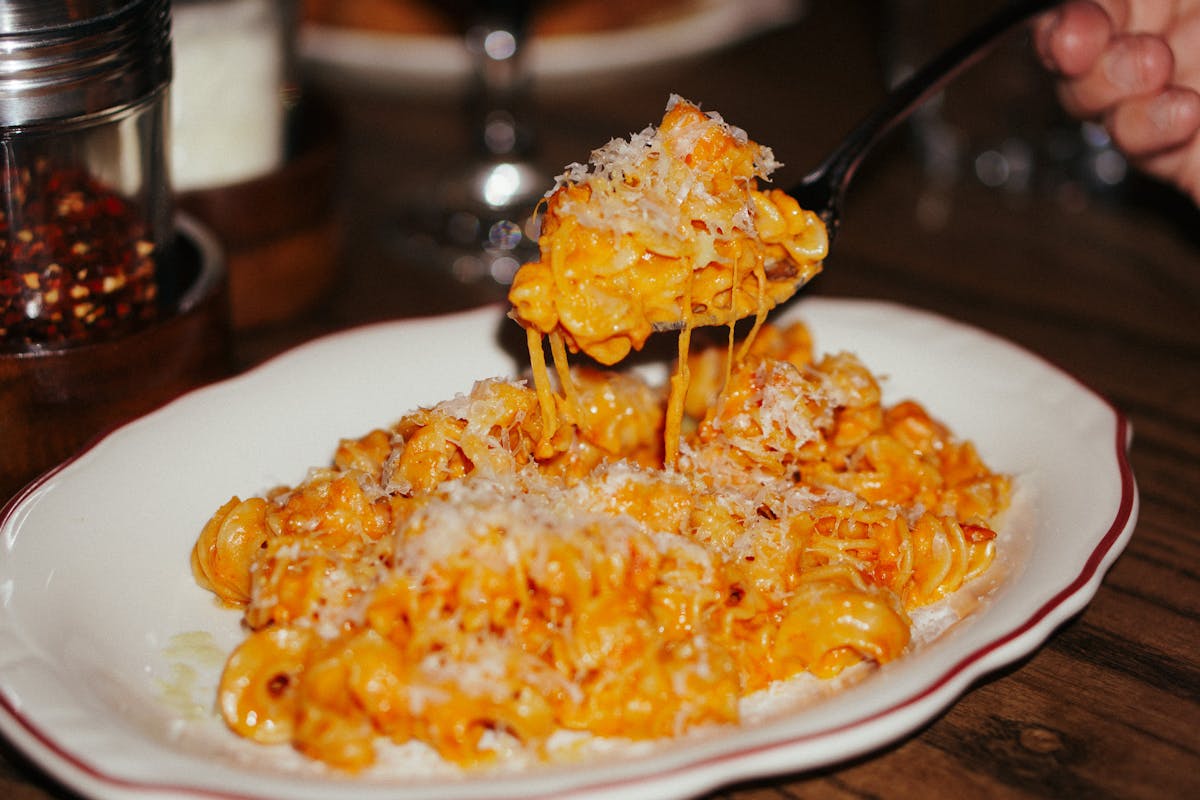 A fork lifts a cheesy bite of creamy pasta covered in rich tomato sauce and fresh Parmesan. The dish looks warm, comforting, and full of classic Italian flavor. It captures the cozy, homemade feel of Pelato.