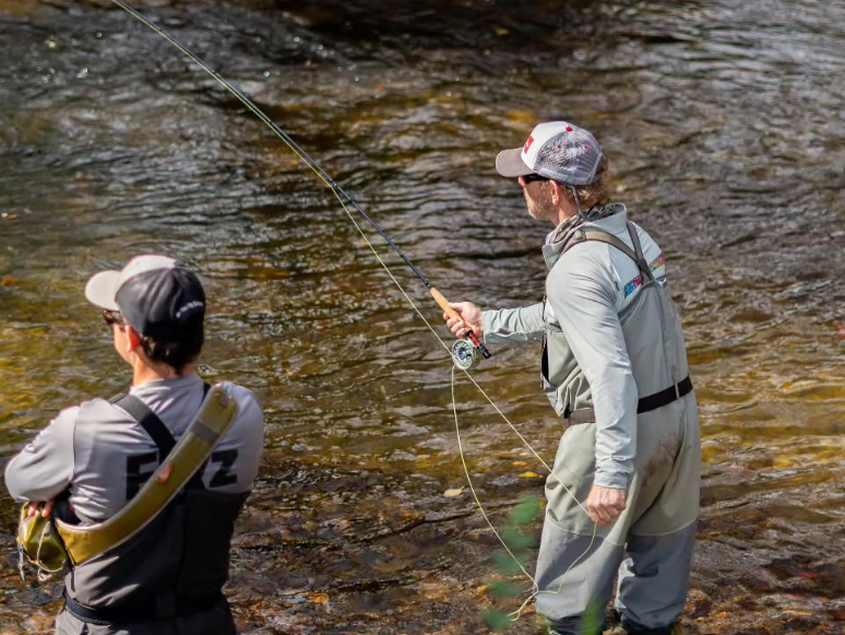 Two men fishing in river with with fishing rod cast in hand