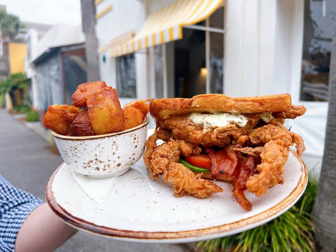A fried soft-shell crab sandwich stacked with bacon and tomato, paired with golden crispy potatoes. A bold Southern twist on a classic sandwich.