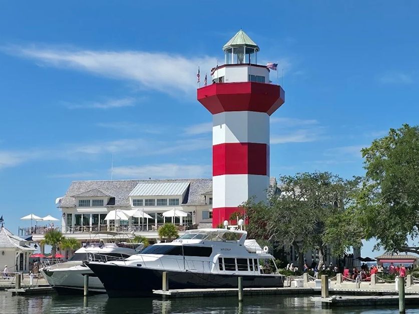 The Harbour Town Lighthouse overlooks a marina filled with boats during a golden Hilton Head sunset. This famous lighthouse and museum offer breathtaking harbor views and a glimpse into local history.