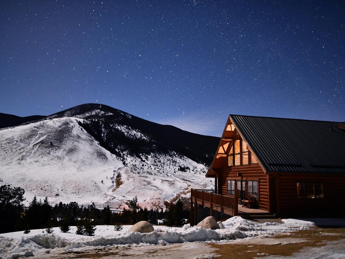 Cabin rental with starry night sky above and mountain in the background covered in snow