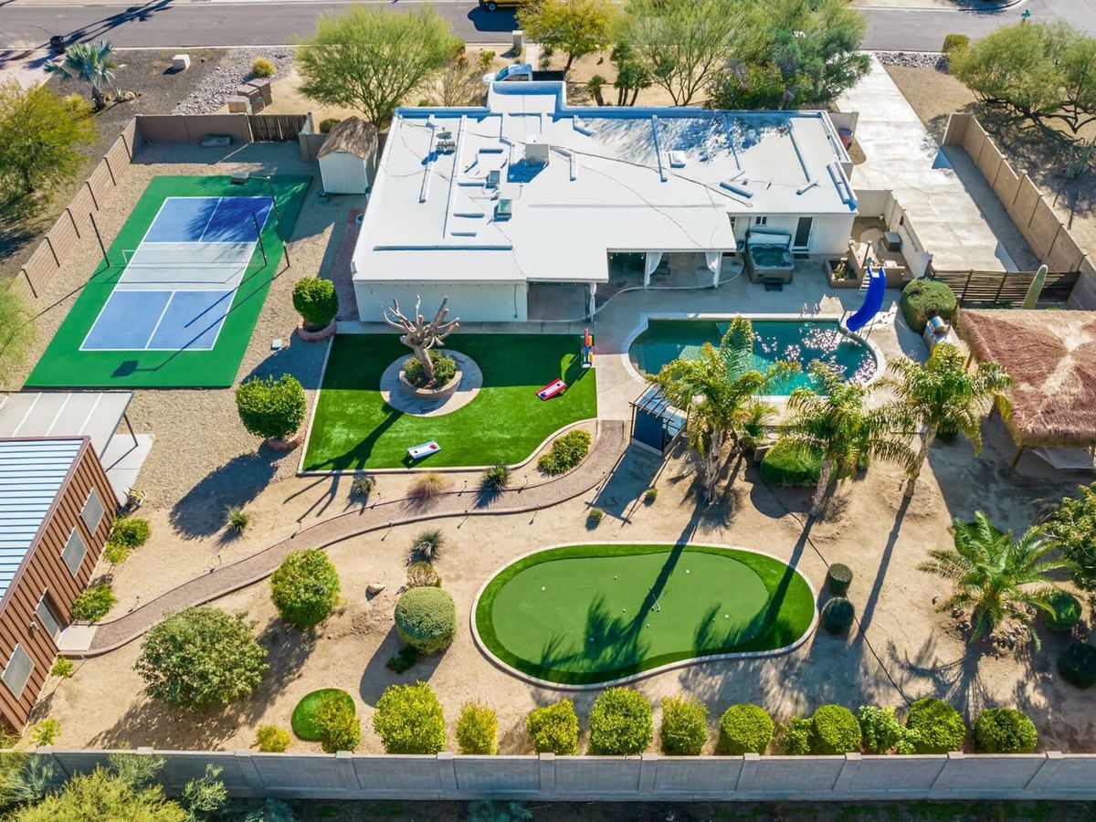 Aerial view of a desert estate featuring a pickleball court, putting green, pool with a slide, and lush landscaping.